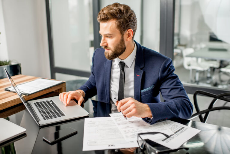 handsome tax manager dressed suit working with documents laptop modern office interior Pinnacle Accounting & Advisory